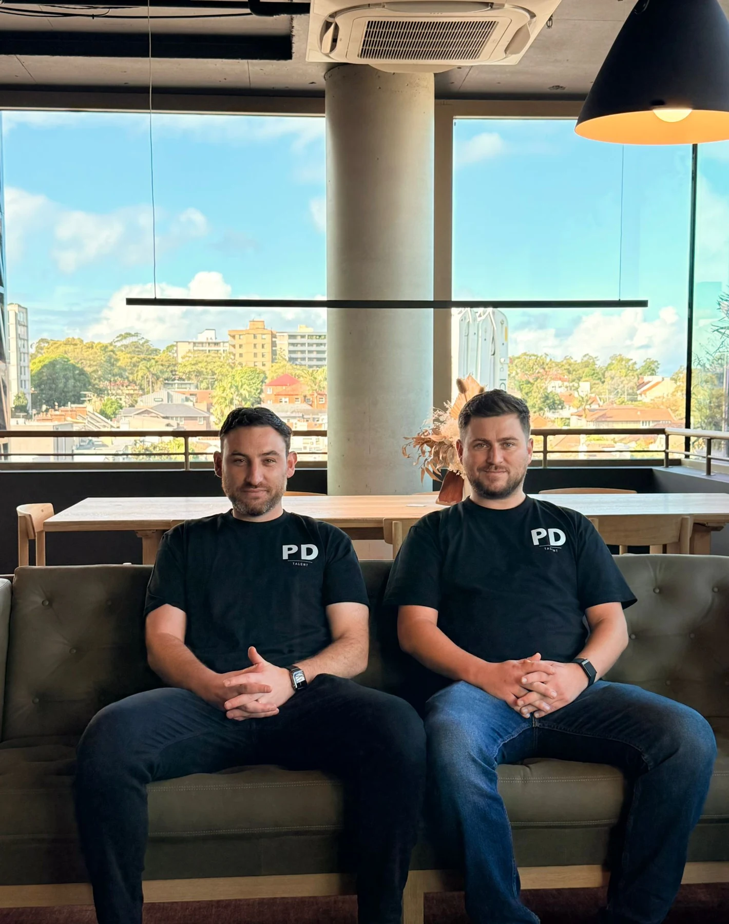 PD Talent founders Sean Donnelly and Lewis Perry sitting together in their branded shirts.